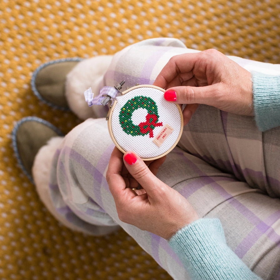 Person holding a small embroidery hoop with a Christmas-themed design on a patterned surface.