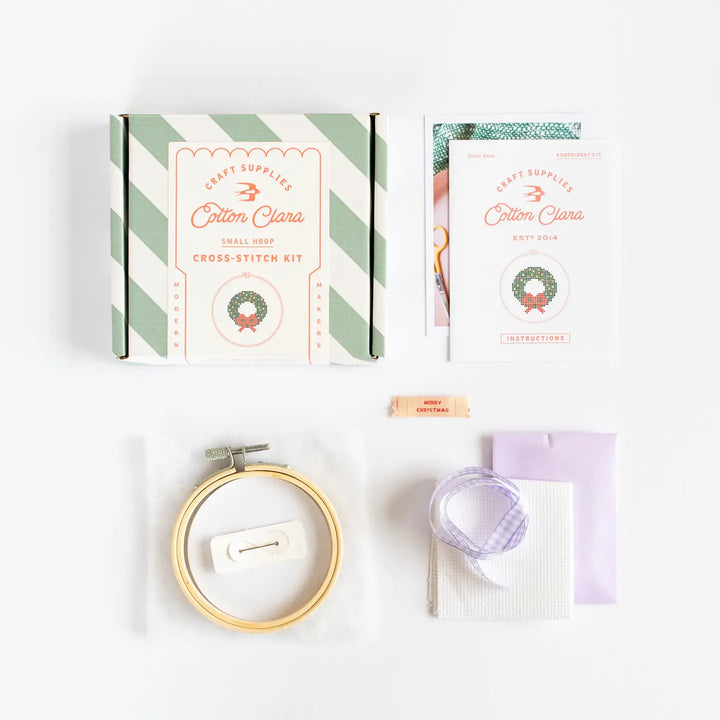 Cross-stitch kit with a box, hoop, and materials on a white background