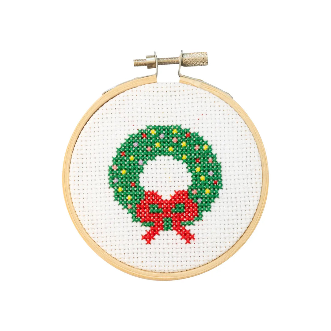 Cross-stitched Christmas wreath with a red bow in a wooden hoop on a white background