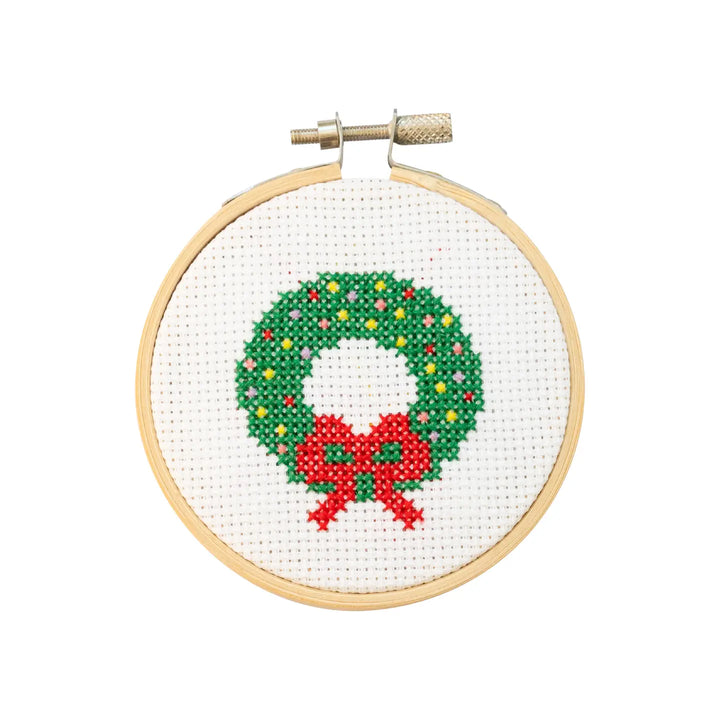 Cross-stitched Christmas wreath with a red bow in a wooden hoop on a white background