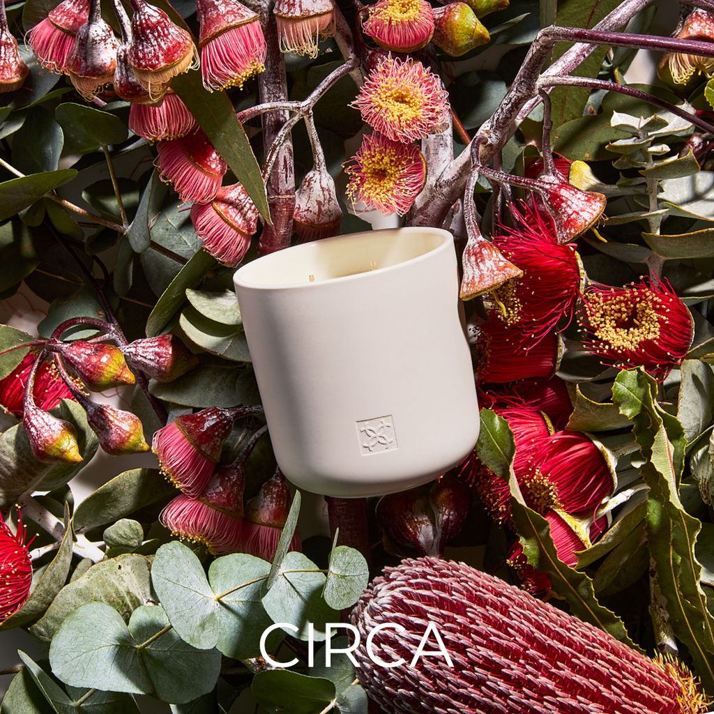 White candle in a decorative container surrounded by red and pink flowers with 'Circa' branding.