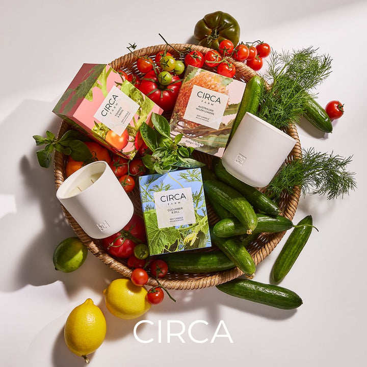 Circa products including candles and boxes on a white surface with fresh vegetables and herbs.