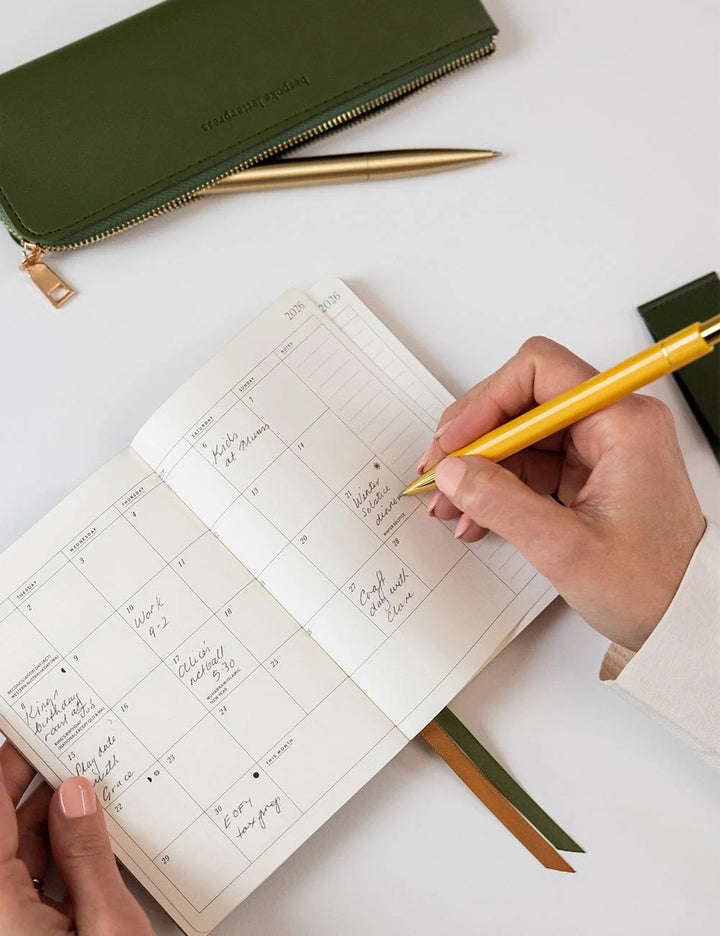 Person writing in a planner with a yellow pen on a white surface
