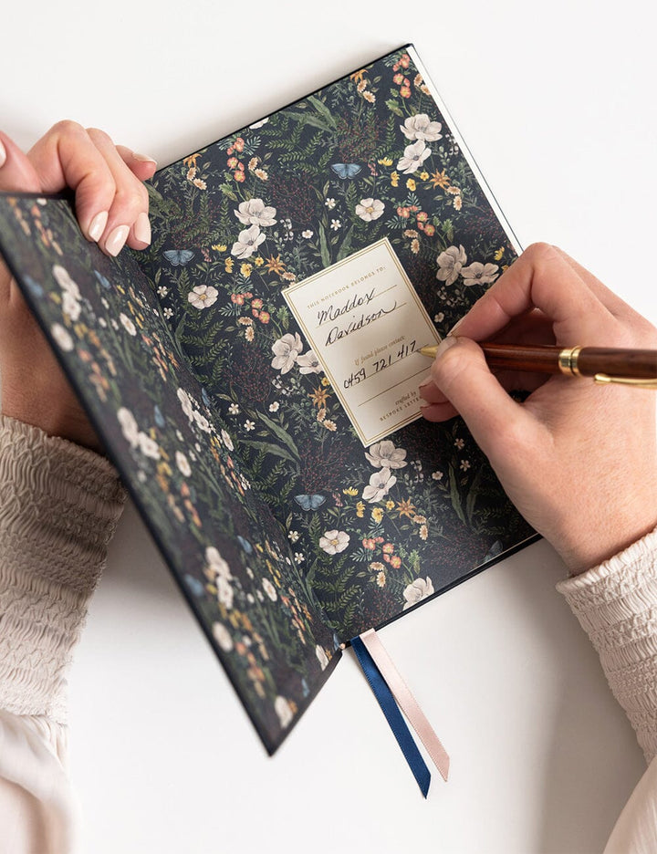 Floral-patterned notebook with a hand holding a pen on a white surface