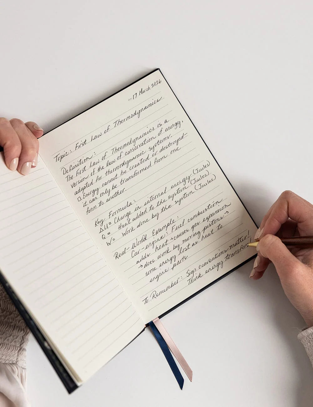 Person writing in a notebook with a pen on a white surface