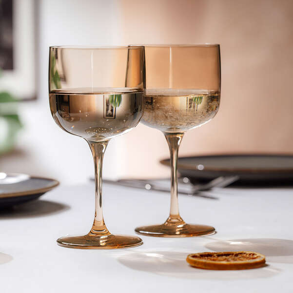 Two amber-colored wine glasses on a white surface with a blurred background