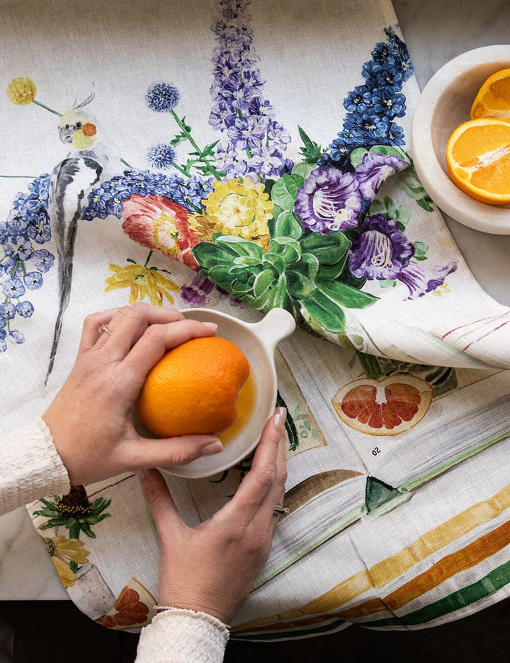 Linen tea towel with flowers a cockatiel on it with somone juicing an orange on it 