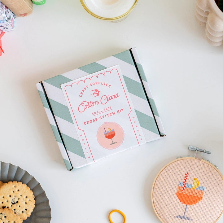 Cross stitch kit box with a small embroidery hoop and cross-stitched design on a white surface.