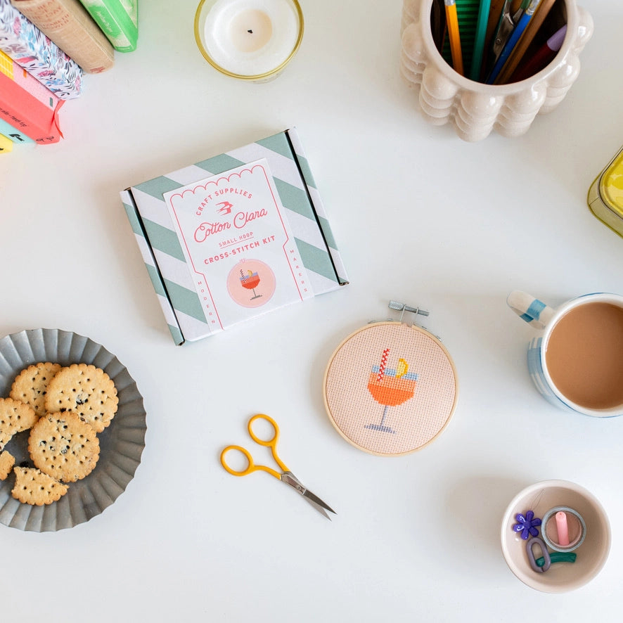 Crafting setup with embroidery hoop, cookies, and coffee on a white surface