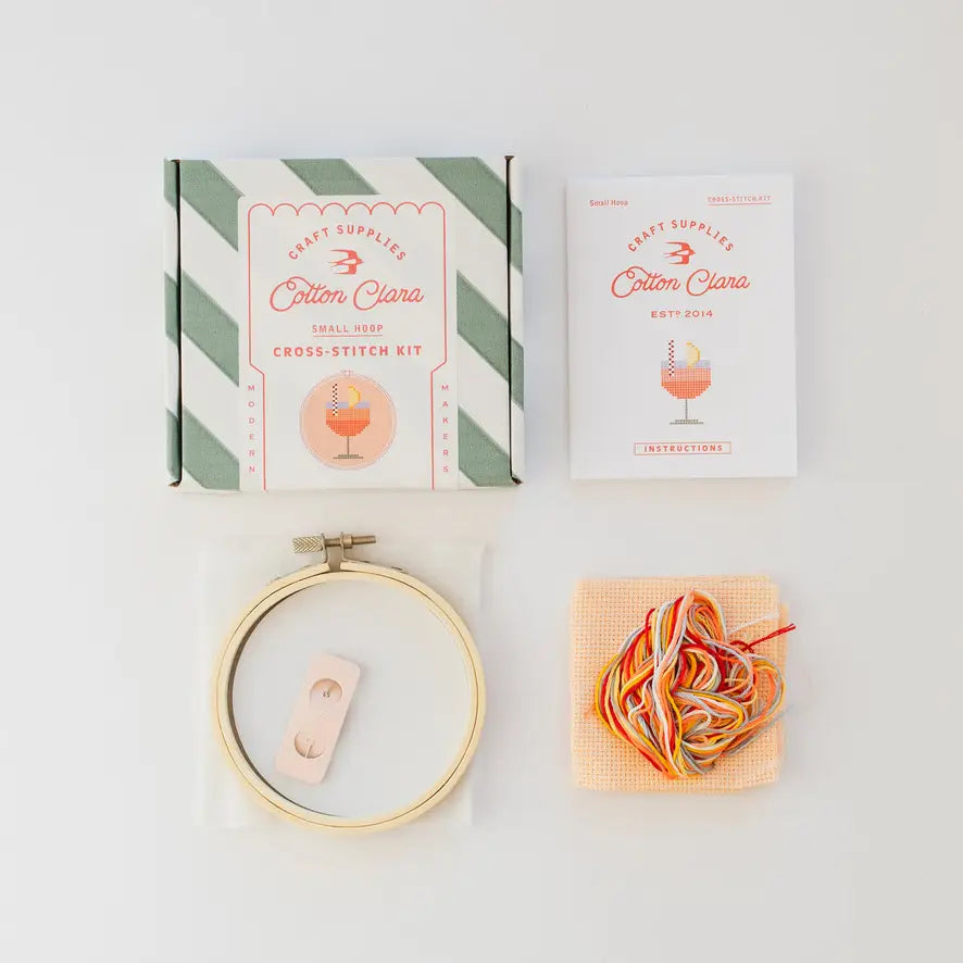 Cross-stitch kit with hoop, thread, and packaging on a light gray background