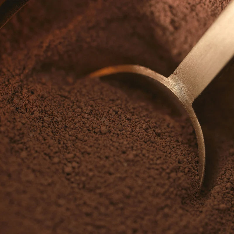 Wooden scoop in a pile of dark brown coffee grounds