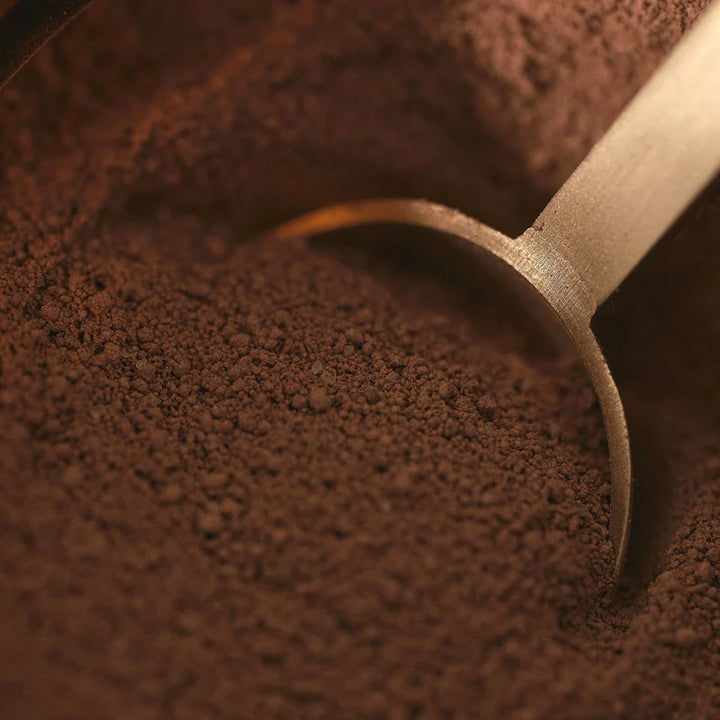 Wooden scoop in a pile of dark brown coffee grounds