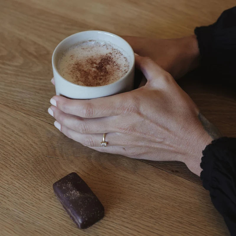 Hand holding a cup of cappuccino with a chocolate bar on a wooden table