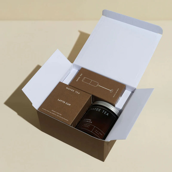 Open box containing a latte cup and a container labeled 'MAYDE TEA' on a beige background