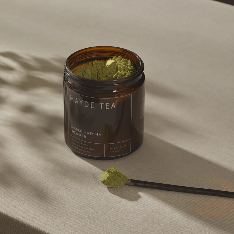 Jar of Mayde Tea maple matcha powder with a spoonful of powder on a beige background