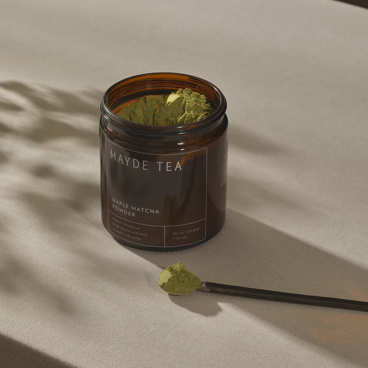 Jar of Mayde Tea maple matcha powder with a spoonful of powder on a beige background
