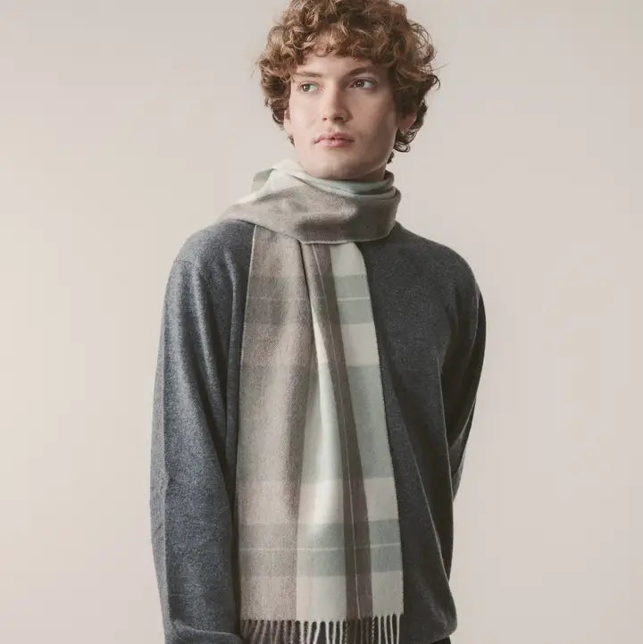 Person wearing a gray sweater and plaid scarf against a plain background