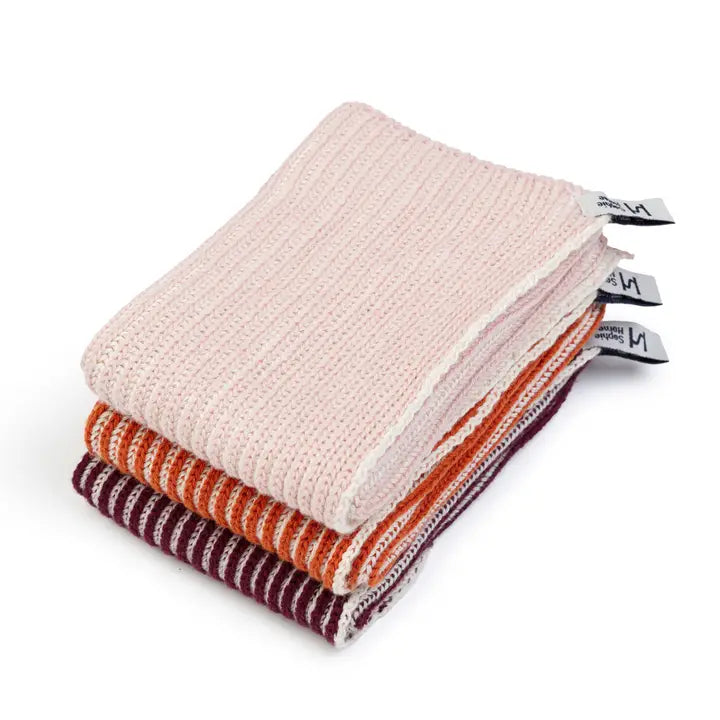 Stack of folded cotton dish cloths in pink, orange, and purple on a white background