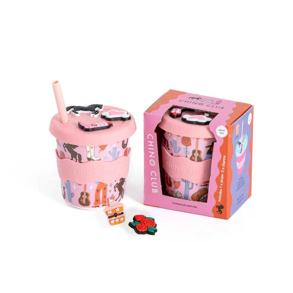 Pink cup with straw and decorative elements next to its packaging on a white background