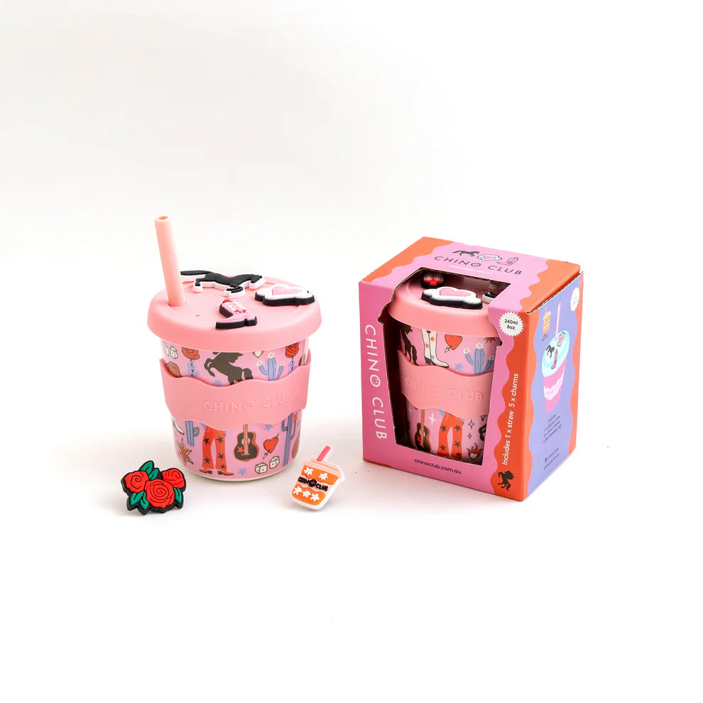 Pink cup with straw and decorative elements next to its packaging on a white background