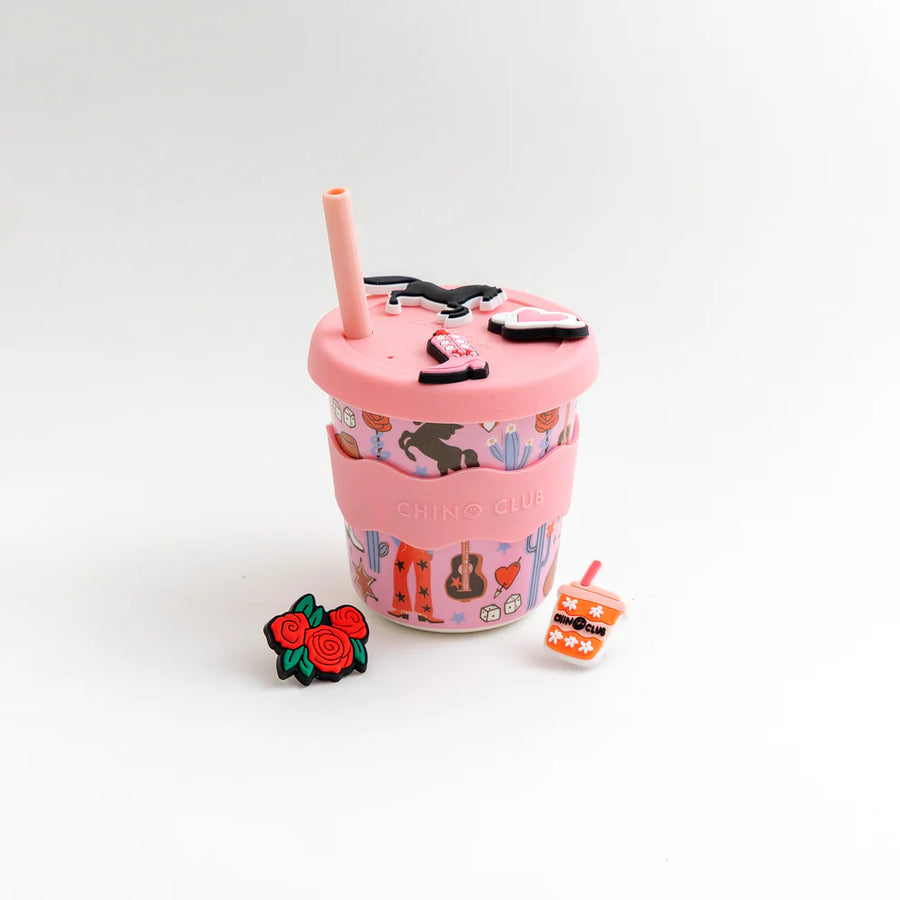 Pink cup with straw, small pink cup with design, and decorative charms on a white background
