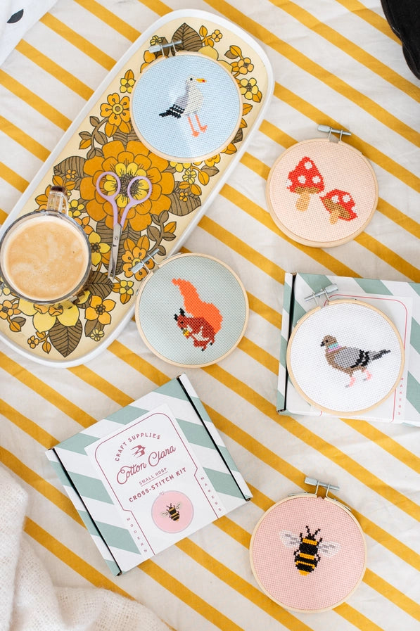 Decorative items including a tray with floral design, small dishes with animal illustrations, and cross-stitch kits on a striped surface.