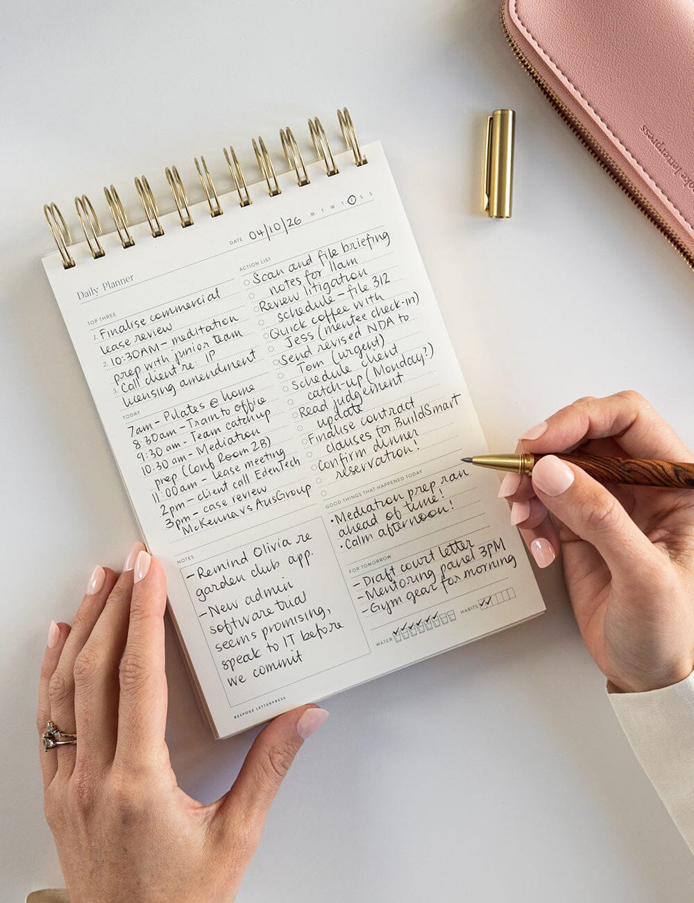 Person writing in a spiral-bound notebook with a pen on a light surface.