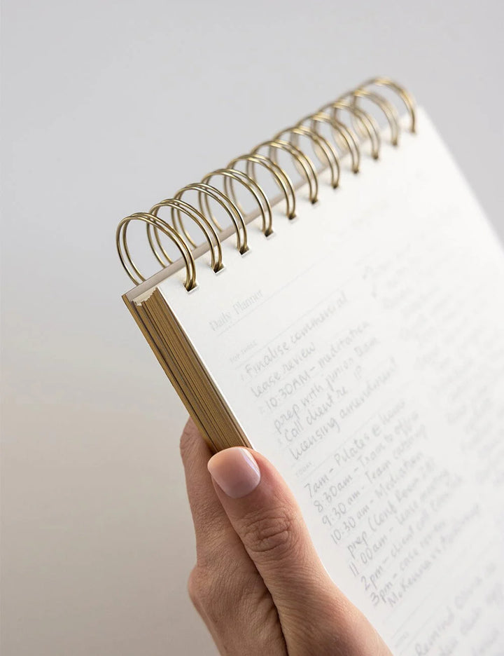 Hand holding a spiral-bound notebook with white pages on a light gray background