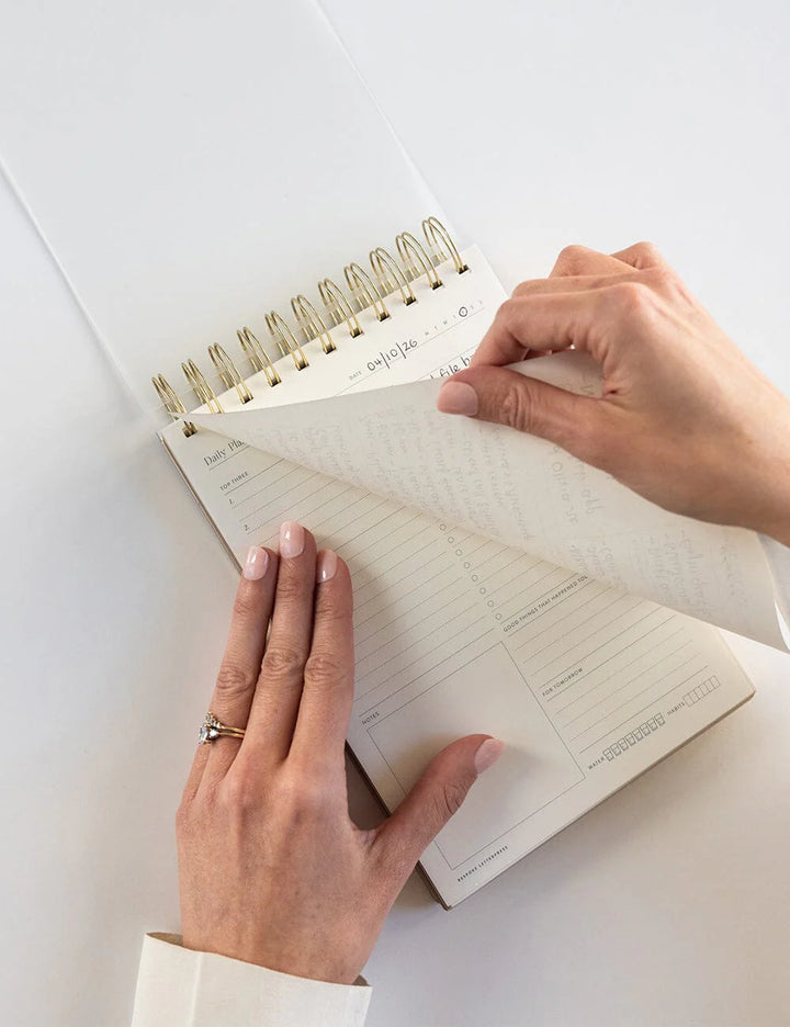 Person holding a spiral-bound notebook with lined pages on a white surface