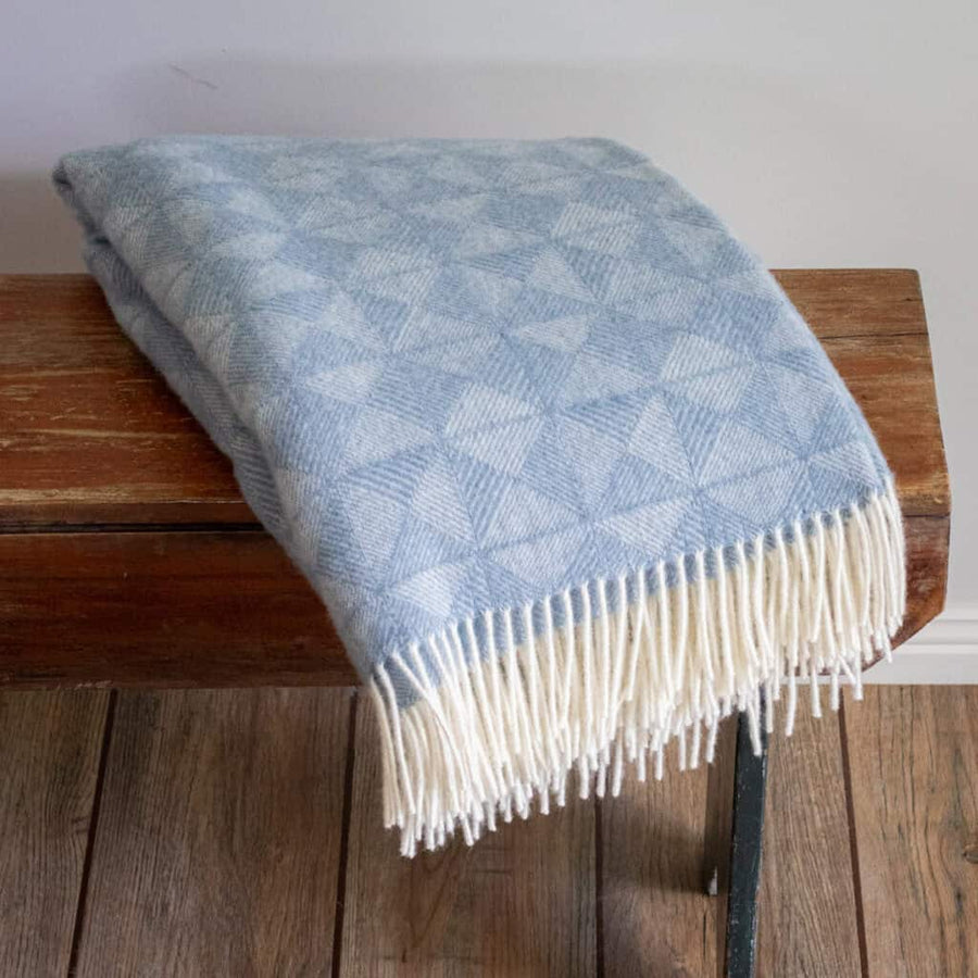 Blue patterned throw blanket with white fringe on a wooden bench.