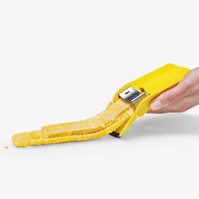 Yellow corn peeler with peeled corn kernels on a white background