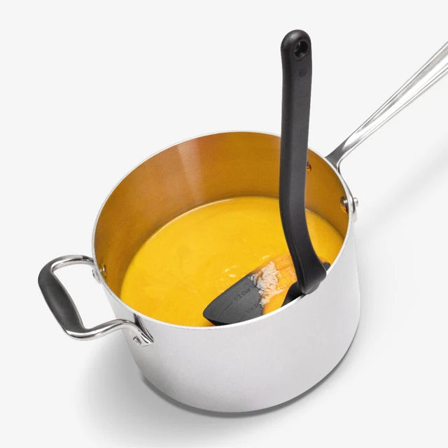 Stainless steel pot with black handled ladle on a white background