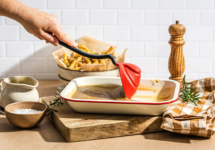 Person serving chips with gravy with a red ladle from a white dish on a wooden cutting board.