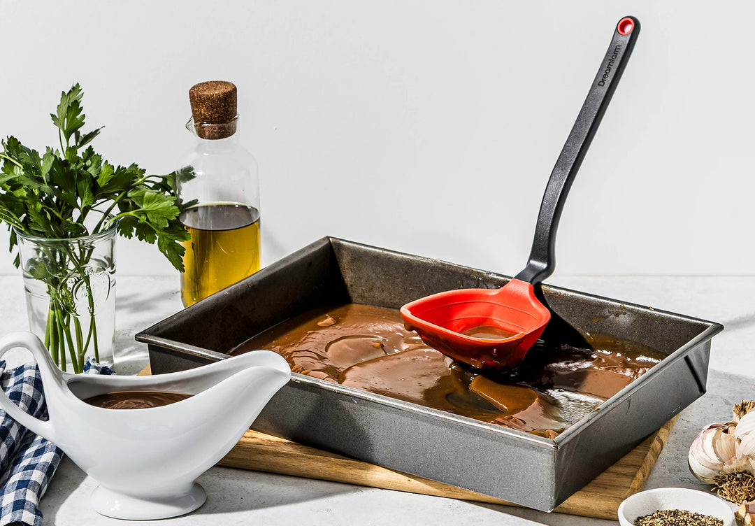 Cooking scene with a roasting pan, spatula, and ingredients on a countertop.