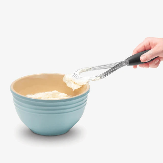 Person using a whisk with cream in a blue mixing bowl on a white background
