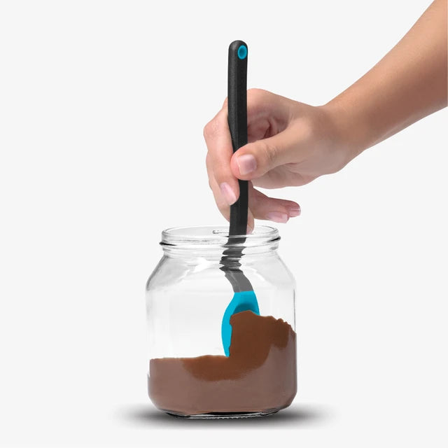 Hand holding a blue spoon with a black handle over a jar of chocolate spread