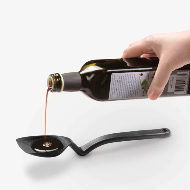 Hand pouring oil from a bottle into a black ladle on a white background