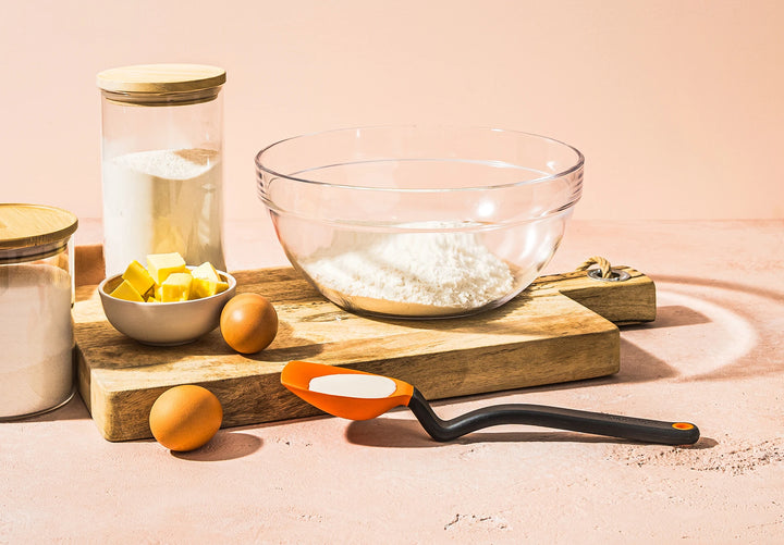 Baking ingredients and utensils on a wooden board with a pink background