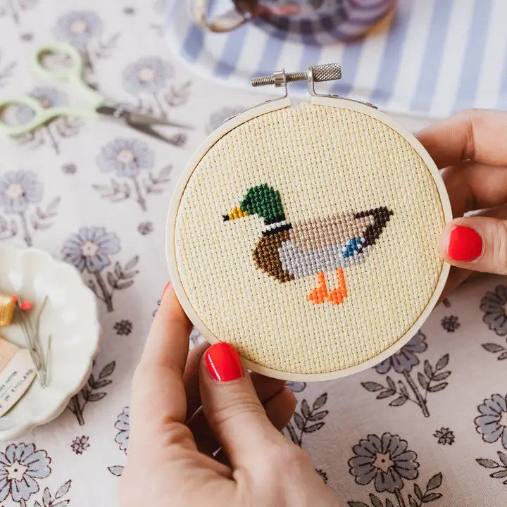 Cross-stitched duck design held in a embroidery hoop on a floral fabric background.