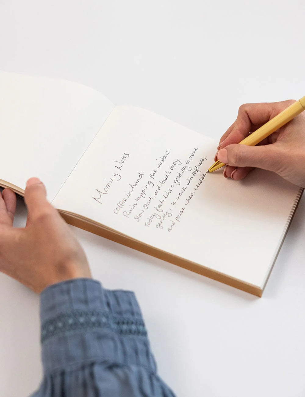 Person writing in a notebook with a yellow pen on a white surface