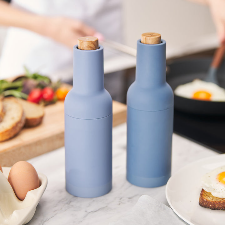 Two blue salt and pepper shakers on a kitchen counter with food in the background.