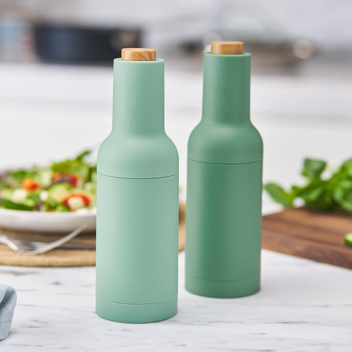 Two green salt and pepper shakers on a kitchen counter with a blurred background