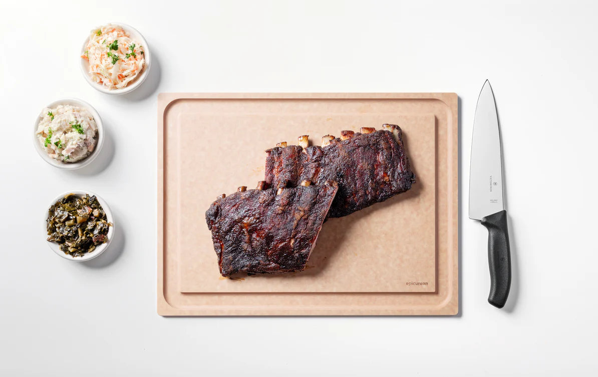 Ribs on a cutting board with side dishes and a knife on a white background