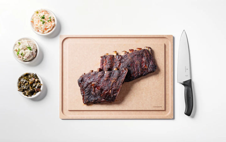 Ribs on a cutting board with side dishes and a knife on a white background