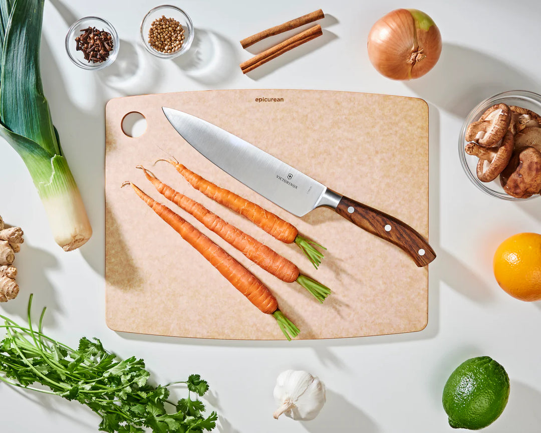 Wooden cutting board with carrots, a knife, and various ingredients on a white surface