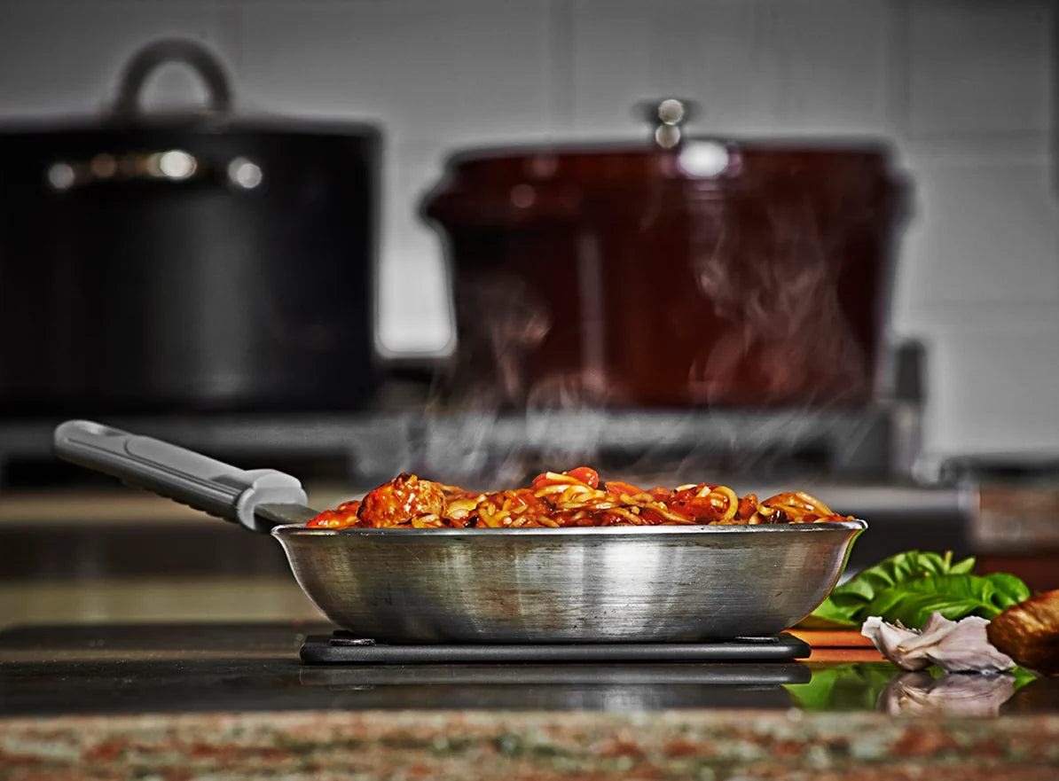 Frying pan with food on a stove, pots in the background