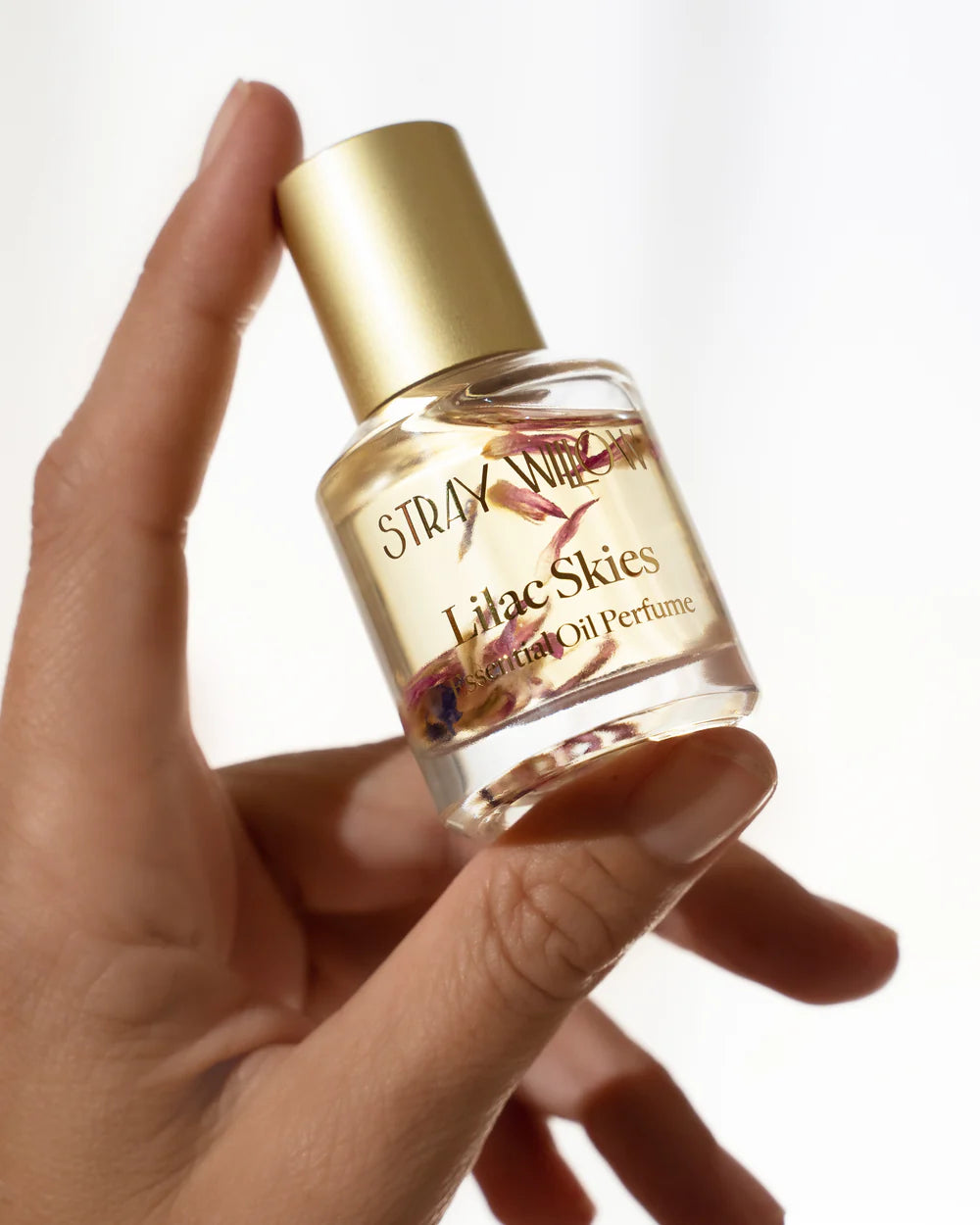 Hand holding a bottle of 'Stray WIllow Lilac Skies' perfume with a gold cap.