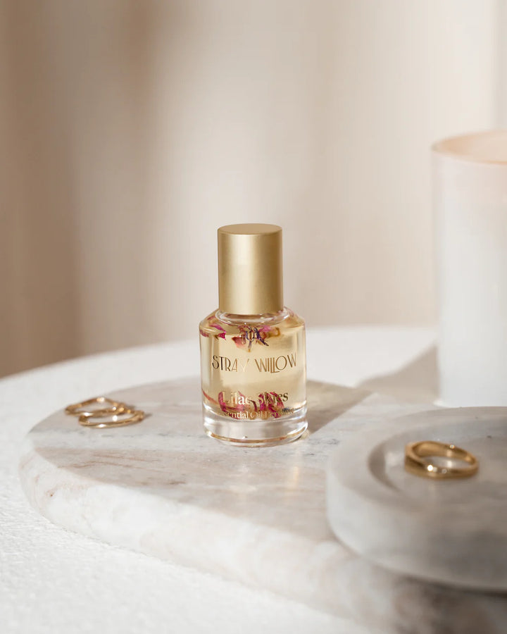 Small bottle of Stray Willow perfume on a marble surface with two gold rings.