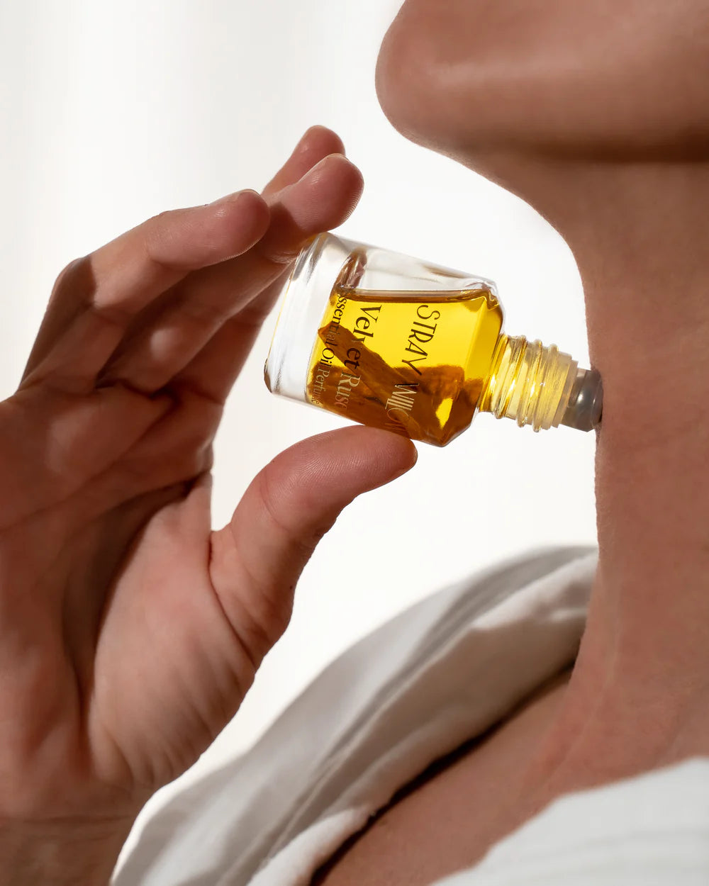 Hand holding a small bottle of perfume against a white background