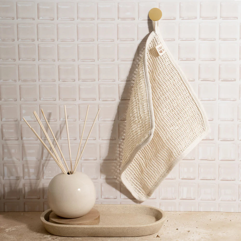 Decorative diffuser with reeds and a woven towel on a tray against a tiled wall.